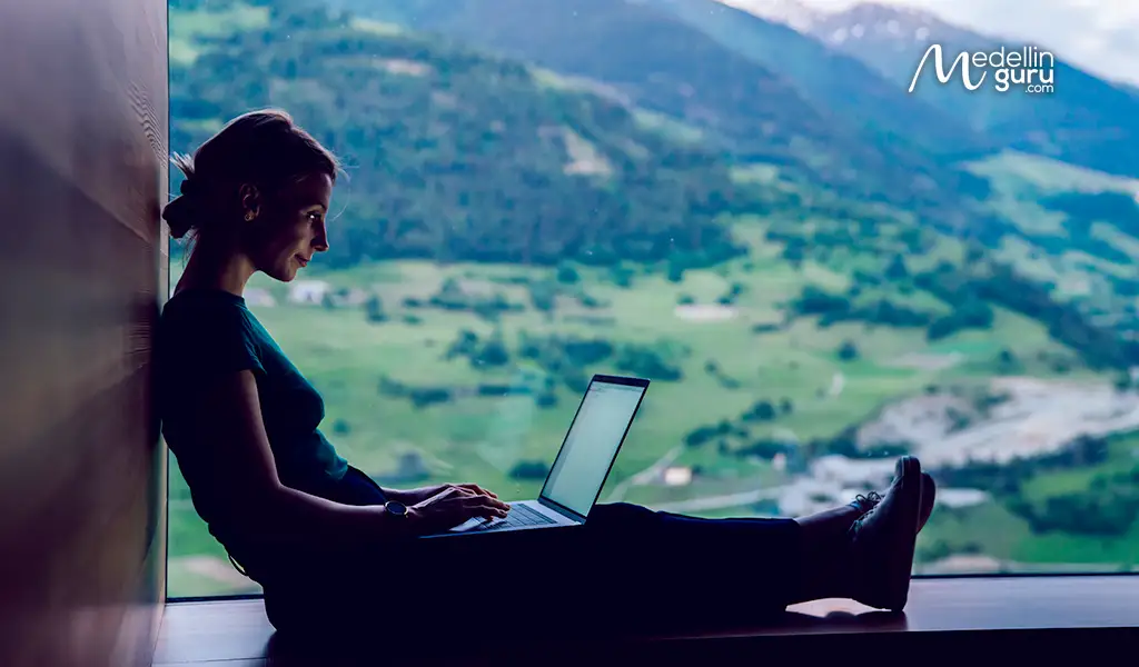 A digital nomad works on their laptop with a view of a lush Colombian landscape