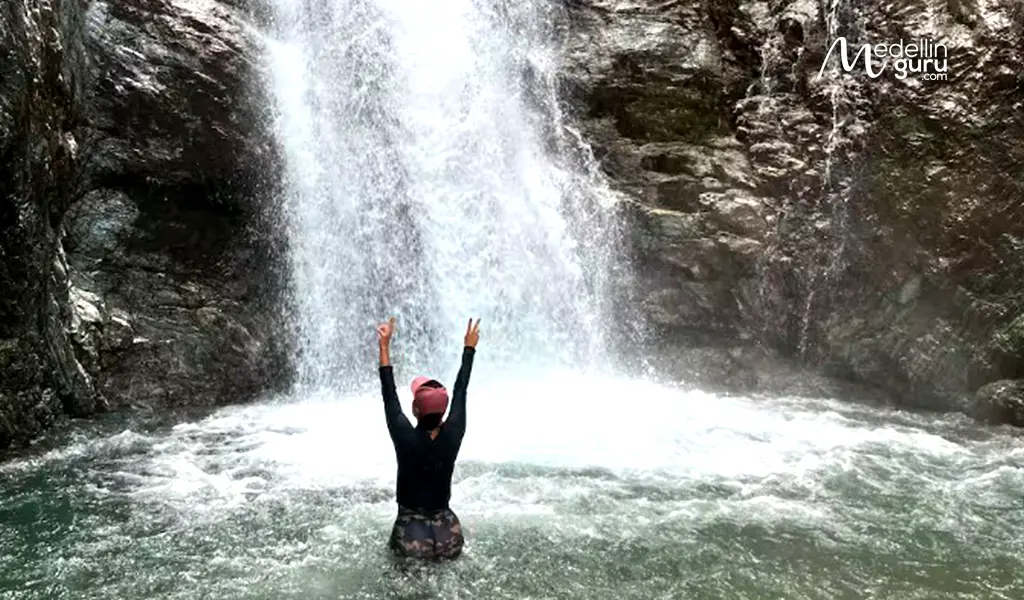 A hiker poses in front of a waterfall in the Colombian mountains