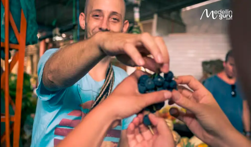 Smiling vendor offering fresh grapes at a bustling fruit market