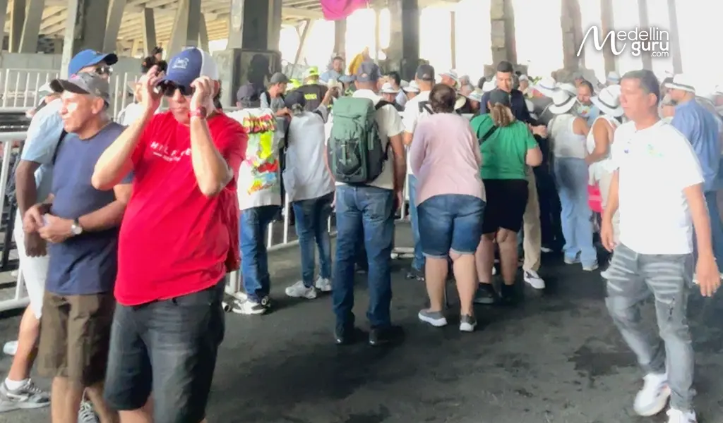 A crowd of enthusiastic attendees waits under an overpass with a banner for the Medellín flower festival, capturing the energy before the Desfile de Silleteros 2025.