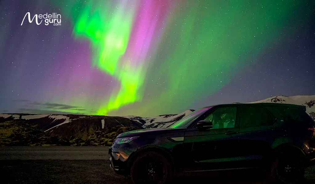 Vibrant green and violet northern lights dancing in the dark sky over the snowy Icelandic countryside.