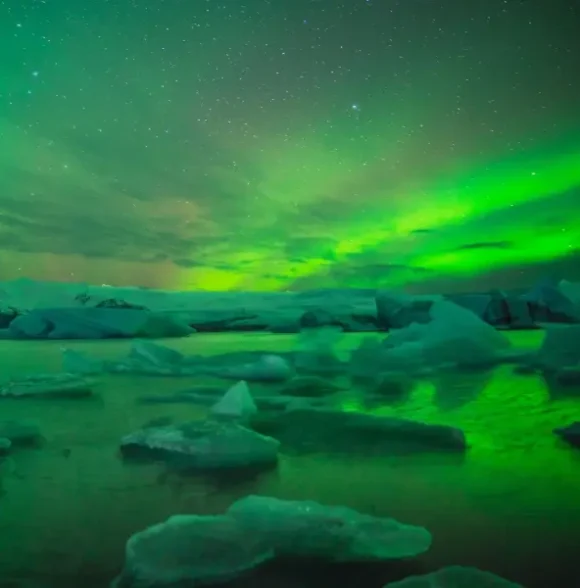 Northern Lights illuminating the night sky over a glacial lagoon in Iceland.